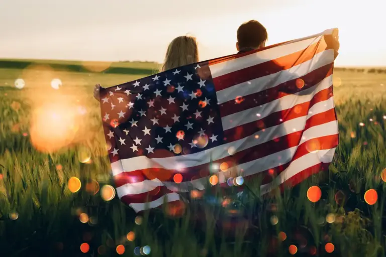 Couple Holding American Flag in Field at Sunset