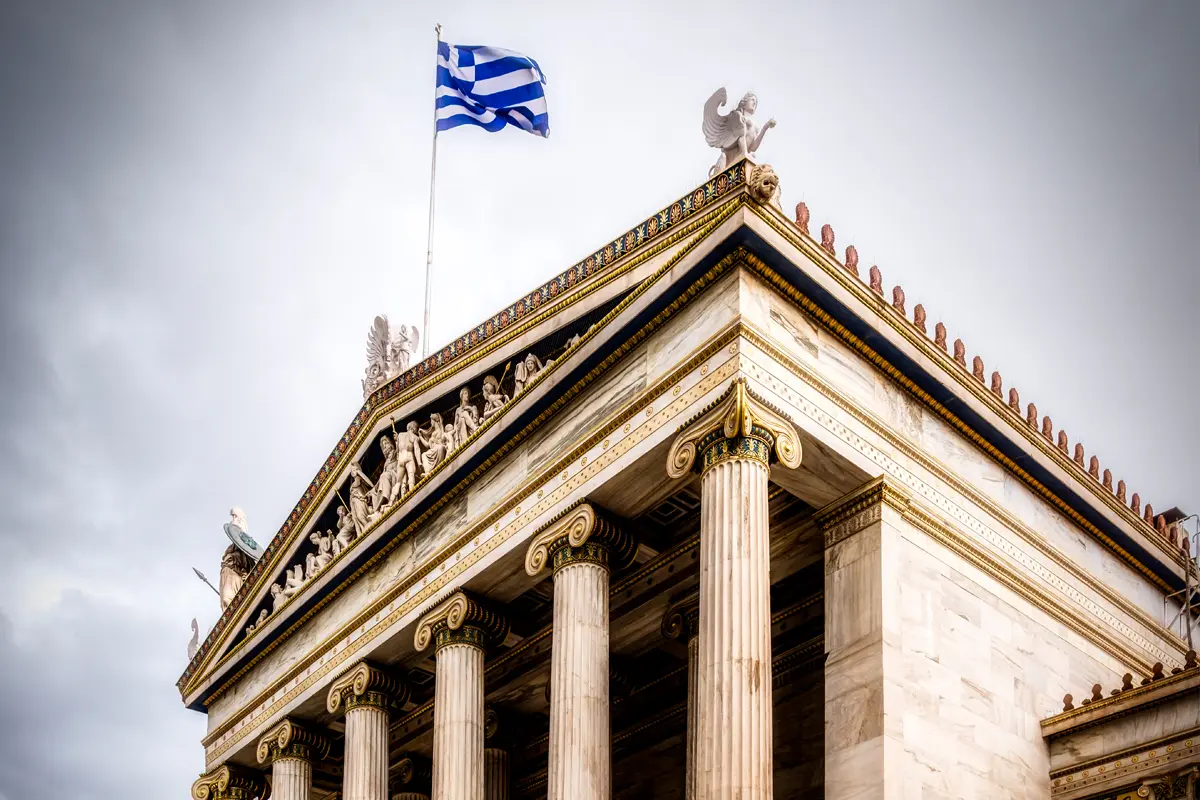 The magnificent National Academy of Athens rises majestically against a cloudy sky.